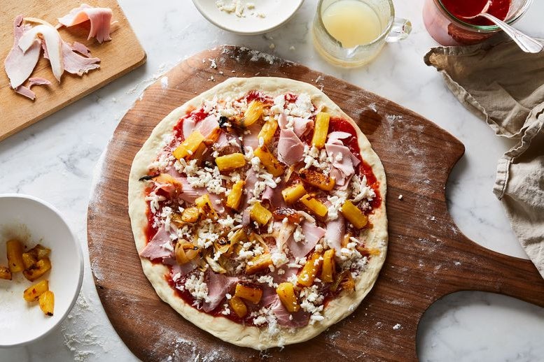 Uncooked Hawaiian pizza with pineapple, ham, cheese, and tomato sauce